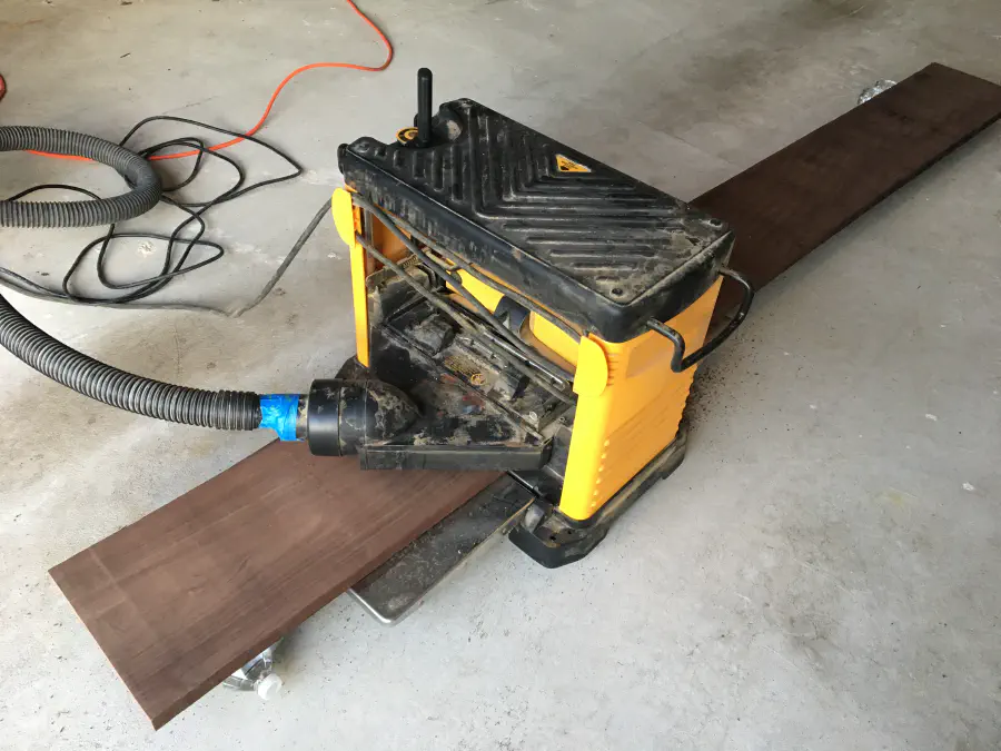 Walnut hardwood board part way through a thickness planer